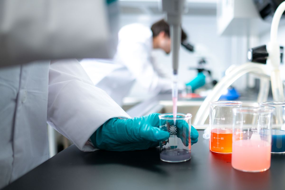 Gloved hand holding a beaker beside laboratory equipment