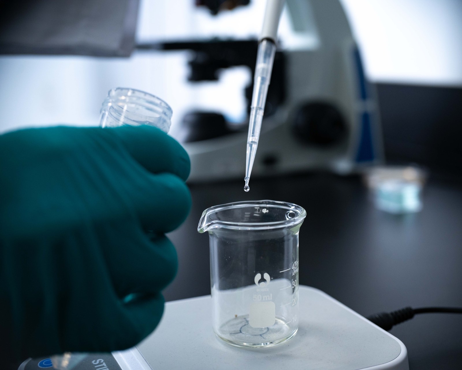 Gloved hands using a pipette above a beaker in a laboratory