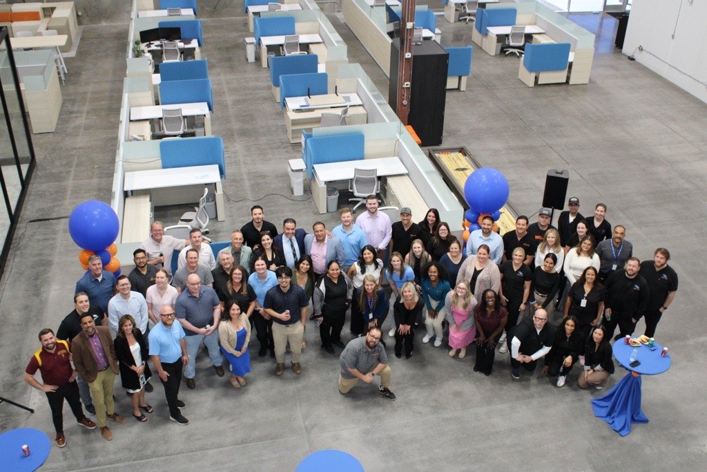 The EmeraNova team gathered for a group photograph in the open-plan office, seen from above, with blue and orange balloons either side